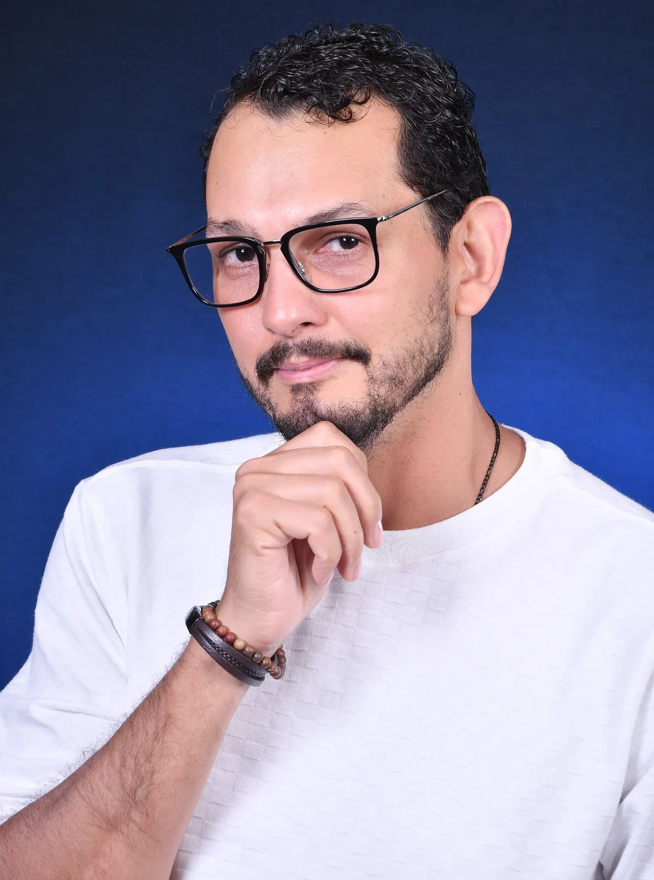 Daniel Pereira in glasses and a white t-shirt, resting his chin on his hand.