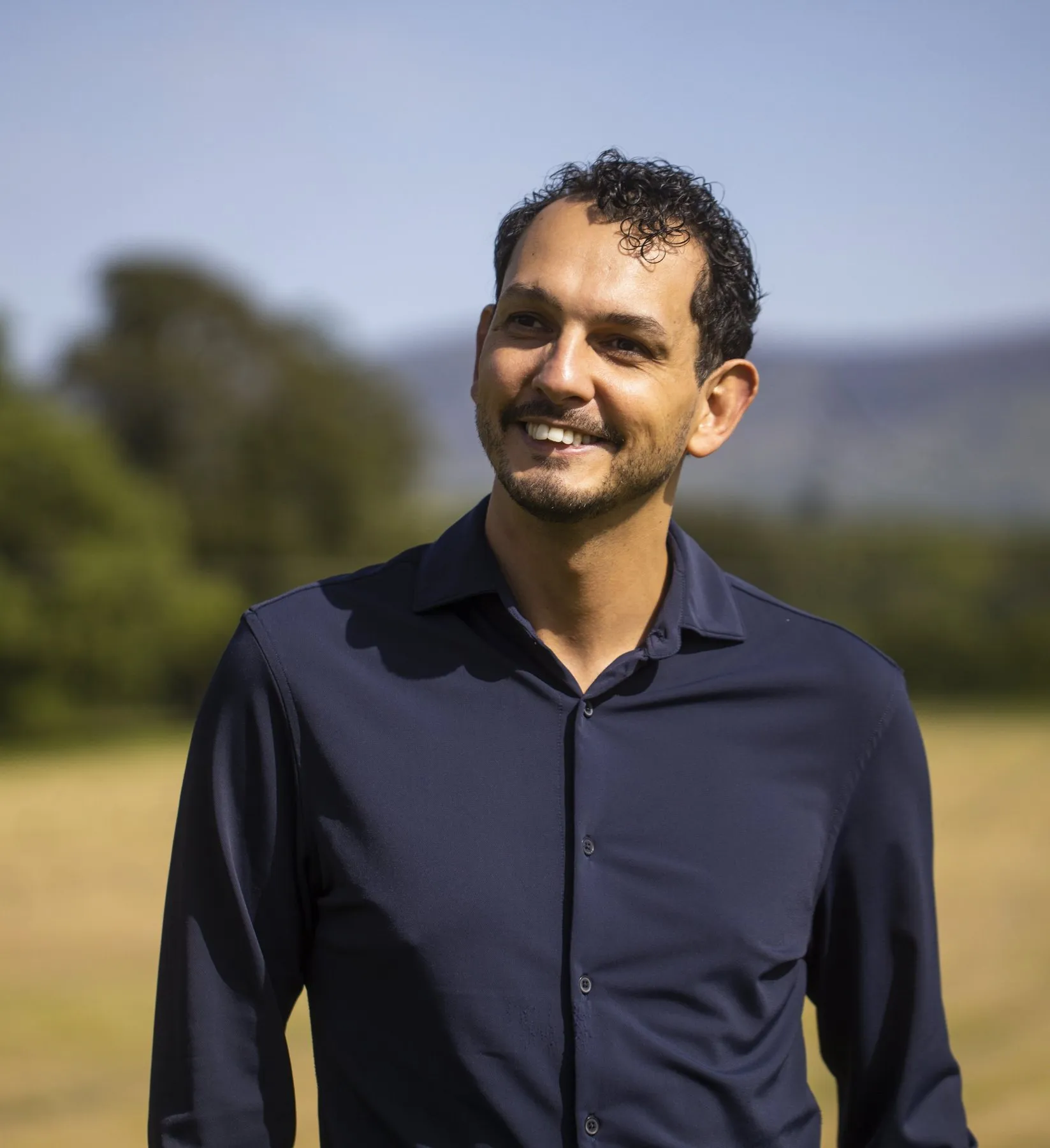 Daniel Pereira smiling and looking off to the side, in a navy shirt, outdoors.
